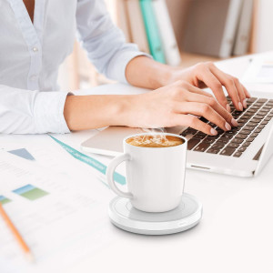 A white mug filled with latte art sits on a sleek white heating coaster, with steam rising from the cup.